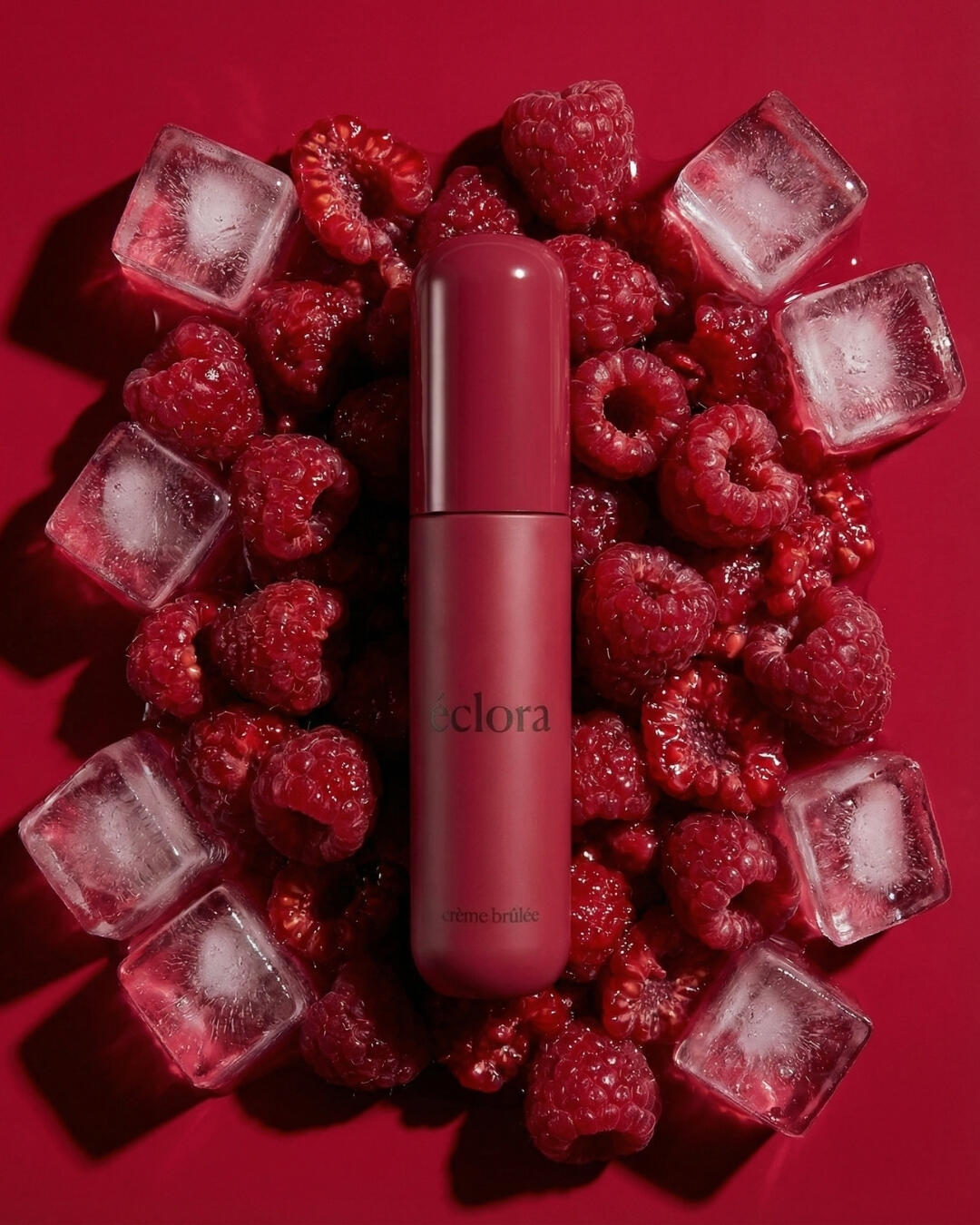 Untitled A dark pink lip tint tube flat layed on top of fresh raspberries and ice cubes