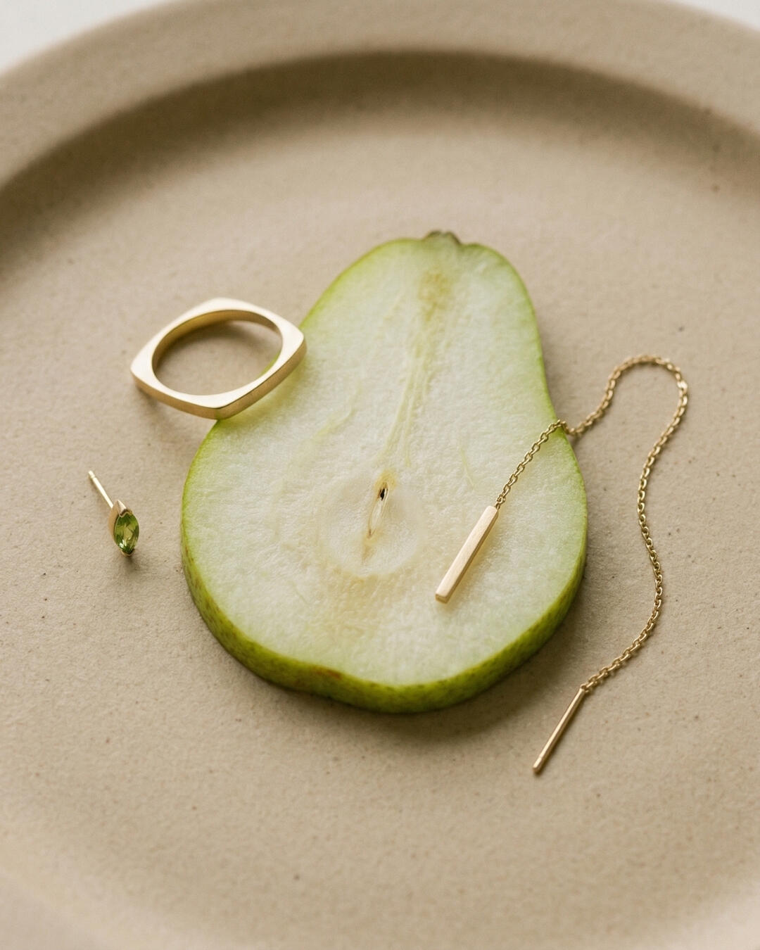 Untitled Diptych product photography display for a minimalist jewelry brand, styling a gold threader earring on a sliced pear.