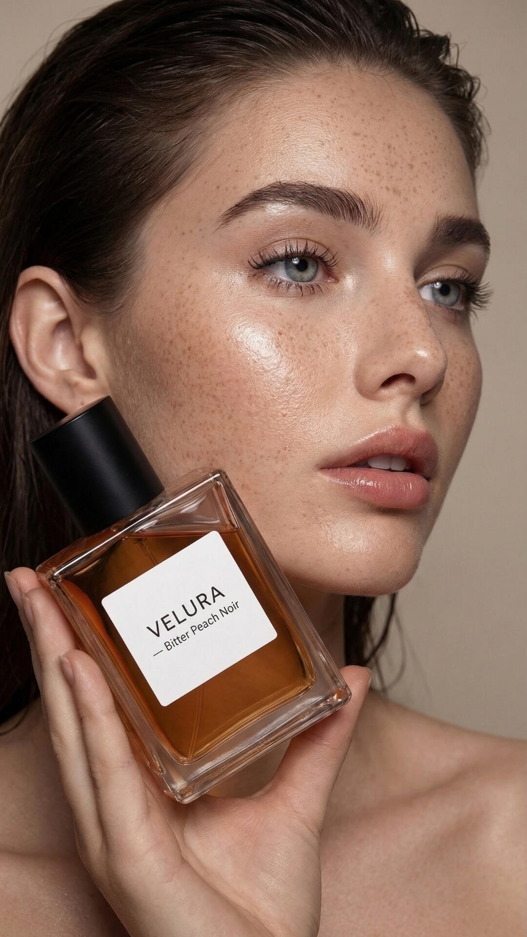 Editorial beauty campaign concept photography, showcasing a close-up portrait of a freckled model with dewy skin holding a minimalist fragrance bottle.